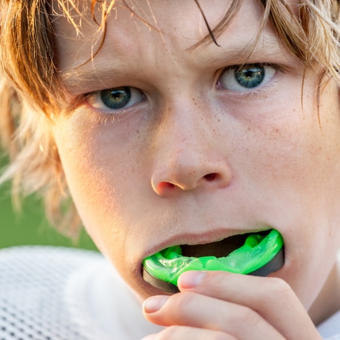 Boy putting green athletic mouthguard into his mouth