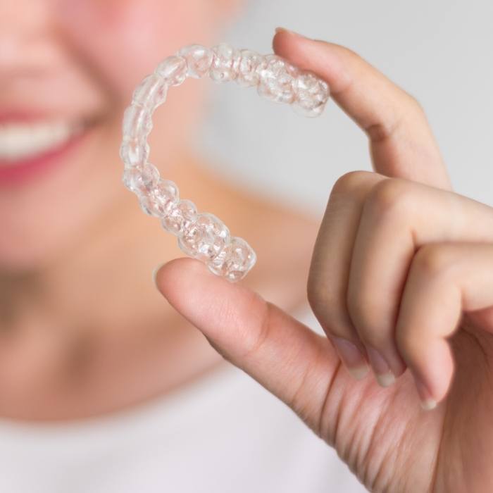 Smiling person holding Invisalign clear aligner