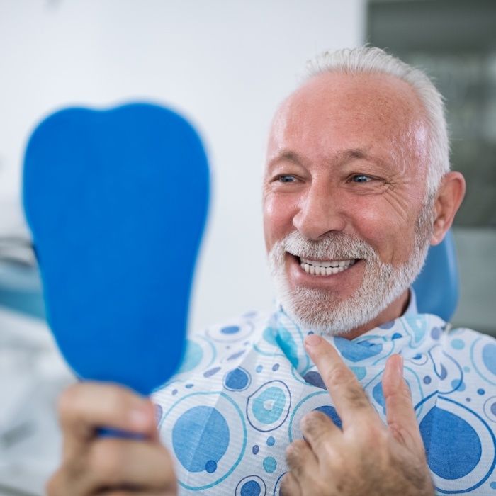 Senior man looking in mirror after smile makeover