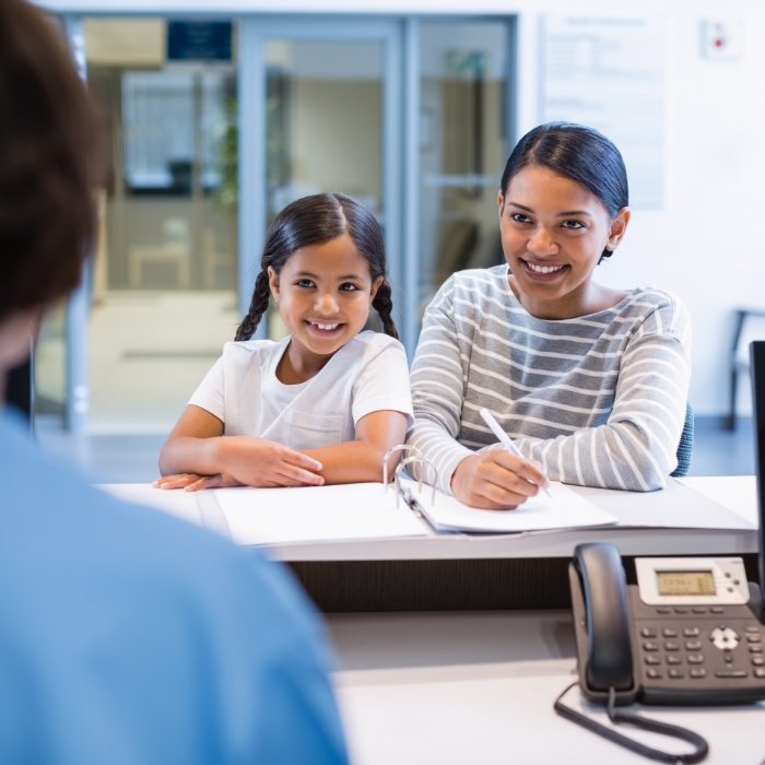 Woman with her child talking to dental team member about dental implant cost