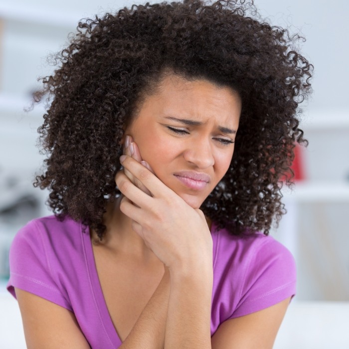 Woman in purple blouse holding her jaw in pain