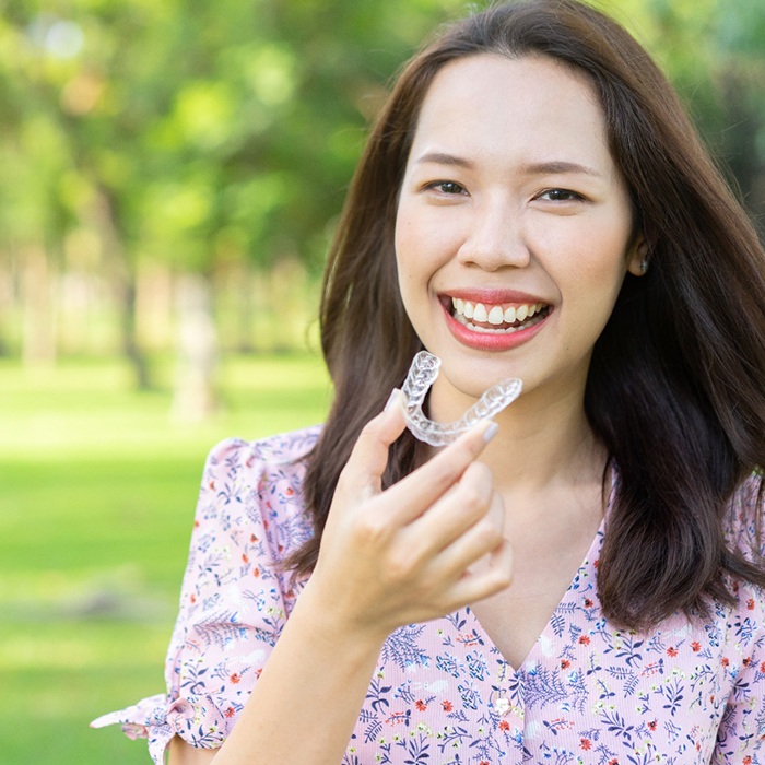 Closeup of woman smiling while putting Invisalign aligner in