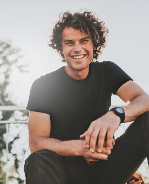 Man with curly brown hair smiling outdoors