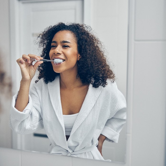 Woman smiling while brushing her teeth in bathroom at home