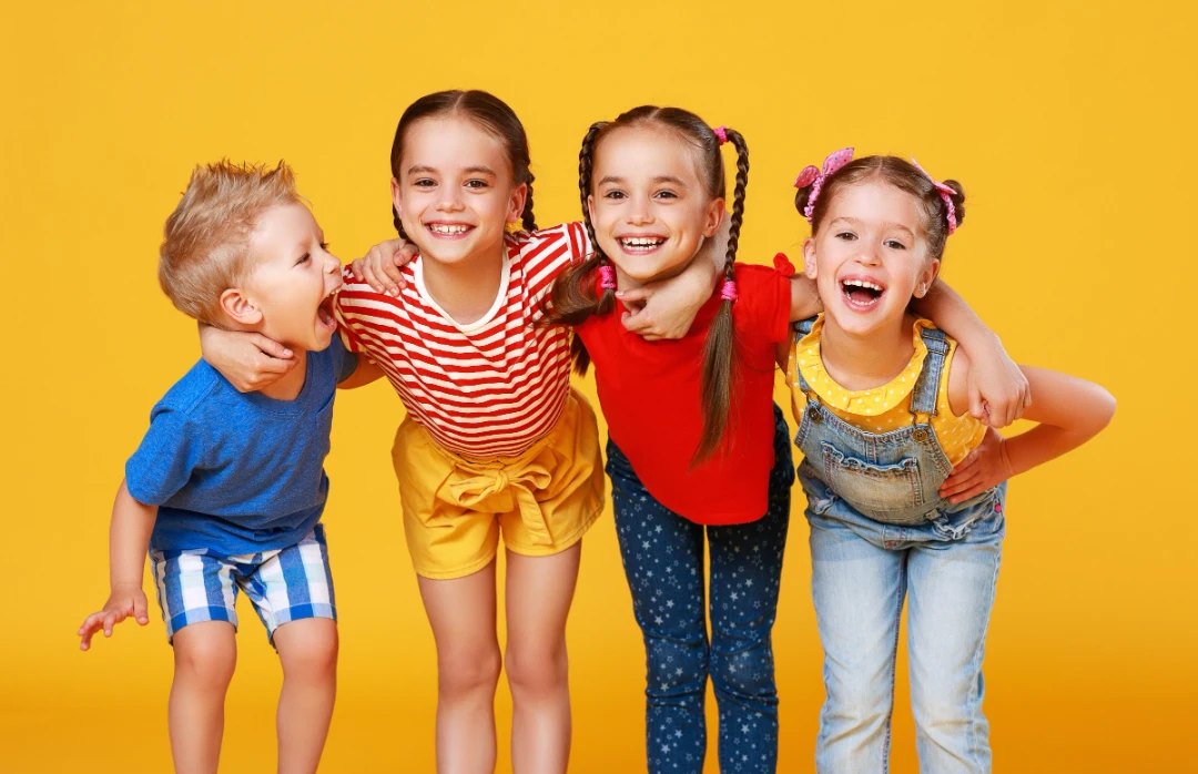 Four smiling children hugging in front of a yellow background